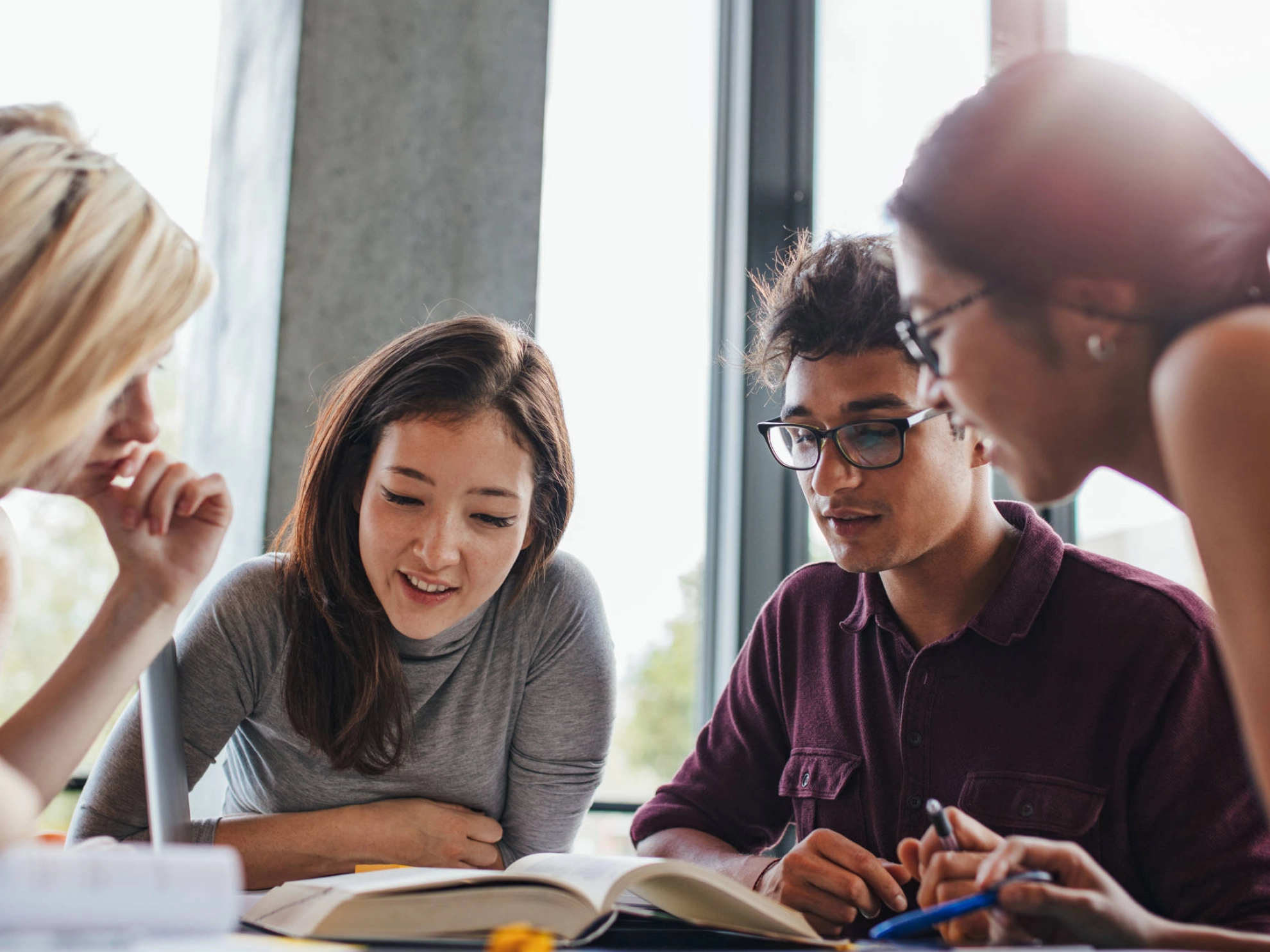 Vier Studierende blicken in Bücher, die vor ihnen auf dem Tisch liegen.