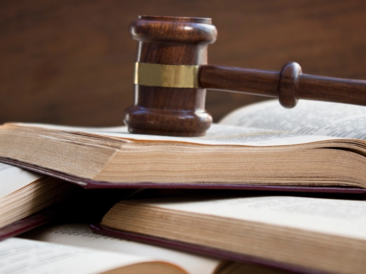 Ein Richterhammer liegt auf geöffnetem Gesetzbuch, mehrere Gesetzbücher liegen darunter